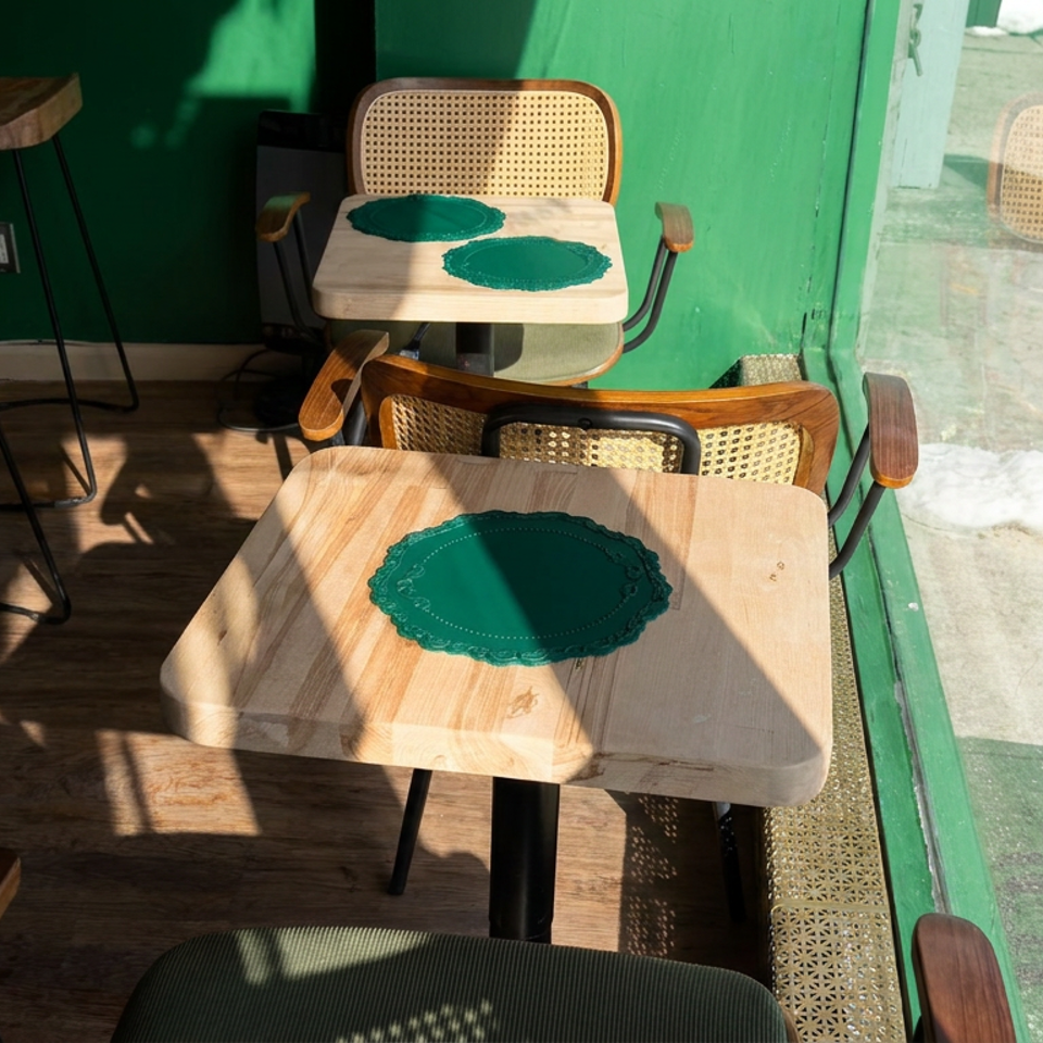 Sunlit restaurant corner with wooden tables, woven chairs, green placemats, and a snowy sidewalk visible through the window.